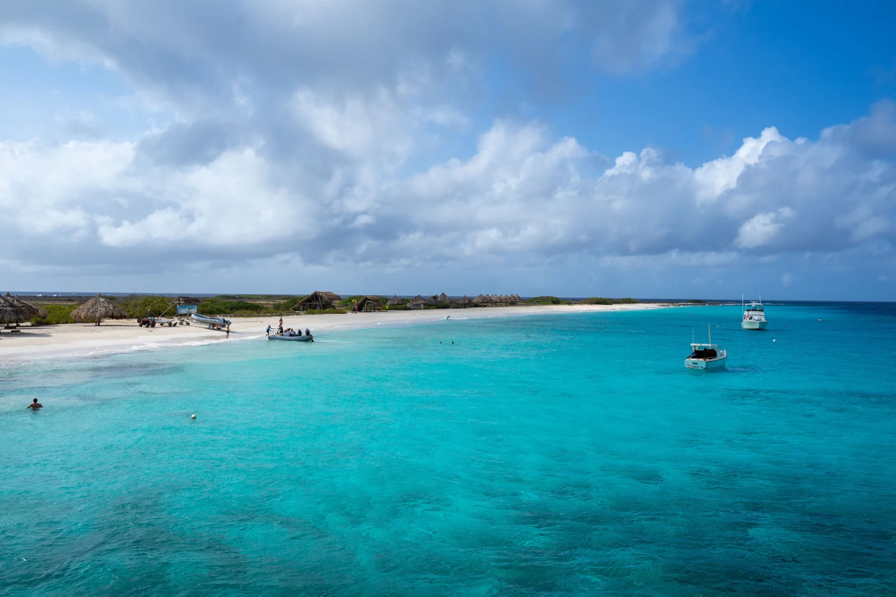 Small boats in clear blue water along a low coastline